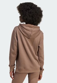 Brown hoodie with a textured finish, featuring a drawstring hood and long sleeves, worn over matching ribbed leggings.