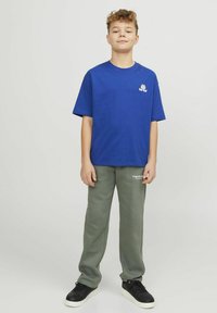 Blauwe katoen t-shirt met een logo op de borst, gecombineerd met grijze joggingbroeken. De outfit wordt aangevuld met zwarte sneakers met witte zolen.