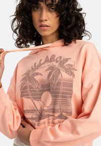 Perzikkleurige hoodie met een grafisch ontwerp van palmbomen en een zonsondergang, voorzien van een relaxed fit en een trekkoord capuchon. Zacht katoenmateriaal.