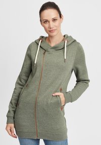 Felpa verde con zip realizzata in tessuto morbido, dotata di cappuccio, coulisse e dettagli accentuati in marrone. Ha tasche laterali e una vestibilità comoda.
