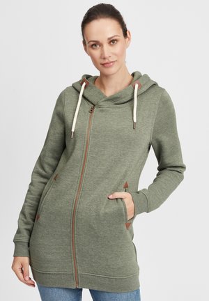 Sweat-zippé vert en tissu doux, doté d'une capuche, d'un cordon de serrage et de détails en brun. Dispose de poches latérales et d'une coupe décontractée.