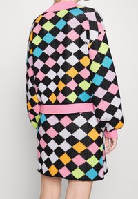 Gebreide trui- en rokset met een zwarte basis en kleurrijke diamantenpatronen in roze, groen, blauw, oranje en witte accenten. Roze kraag en zoom.