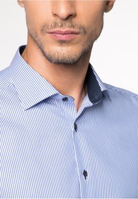 Herrenhemd mit vertikalen blauen und weißen Streifen, gebuttonter Kragen und kontrastierendem marineblauen Innenkragen mit gepunktetem Muster.