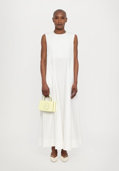 Vestido maxi branco sem mangas de corte largo, combinado com uma pequena mala amarela com um logótipo e elegantes sapatos brancos com salto bloco.