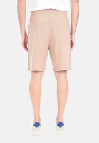 Shorts beige, fino al ginocchio, con un elastico in vita. Tessuto leggero, caratterizzato da una superficie liscia e un design semplice. Indossati con scarpe bianche e blu.
