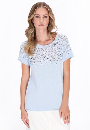 Top de punto azul claro con un patrón de encaje, combinado con una falda larga blanca con una abertura frontal, usado con botines negros de cordones.