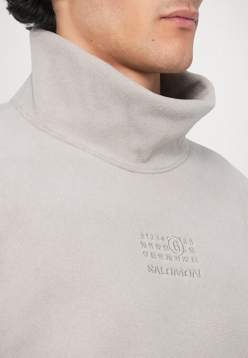 Light gray fleece pullover with a high collar. Features embossed numbers and brand logo. Soft texture, minimal stitching detail.