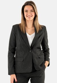 Blazer negro de rayas con un corte ajustado, cierre de un solo botón y dos bolsillos frontales, combinado con una camisa blanca de cuello en V.