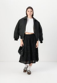 Doudoune noire, crop top blanc, jupe noire à volants, sac noir et chaussures à motif animal avec des chaussettes blanches ; tissu texturé et design superposé.