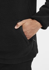 Czarny polarowy sweter z miękkim, teksturowanym wykończeniem, z boczną kieszenią i elastycznymi mankietami dla idealnego dopasowania.