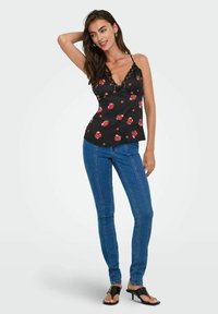 Camiseta sin mangas negra con estampado floral, con tirantes finos y adornos de encaje, combinada con jeans ajustados azules que presentan costuras verticales y un ligero estiramiento.