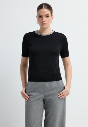 Zwarte korte mouwen gebreide top met een glinsterend effect, met een versierde halslijn. Gecombineerd met grijze op maat gemaakte broek.