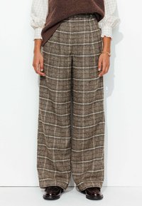 Pantalons à jambes larges en tissu écossais brun, pr�ésentant une surface texturée et un design taille haute. Complétés par des chaussures foncées.