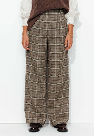 Pantalons à jambes larges en tissu écossais brun, présentant une surface texturée et un design taille haute. Complétés par des chaussures foncées.