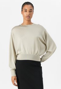 Helles beige, kurzes Sweatshirt mit langen Ärmeln, geripptem Saum und glatter Textur, kombiniert mit einem schwarzen Rock.