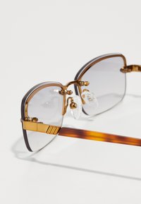 Ochelari transparenți cu ramă din metal auriu, lentile dreptunghiulare și brațe din scoică maro cu accente decorative.