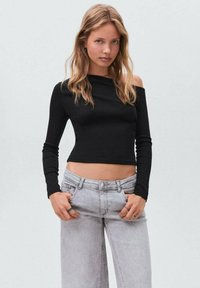 Schwarzes, langärmeliges, kurzes Oberteil mit schulterfreiem Design, kombiniert mit hellgrauen, weit geschnittenen Jeans mit vorderen Taschen.