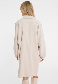 Beige Kordhemdkleid im Oversized-Stil mit Kragen und überschnittenen Schultern, langen Ärmeln und gerader Schnitt bis zur Mitte des Oberschenkels.