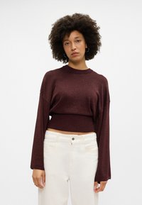 Suéter curto cor bordô com bainha canelada e mangas largas, feito de um material ligeiramente brilhante; combinado com calças brancas de perna reta.