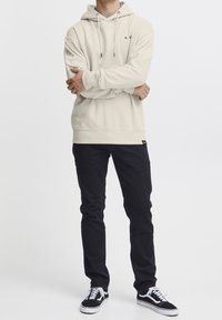 Sweat à capuche couleur crème avec une poche kangourou, associé à un jean foncé slim et des baskets noires et blanches.
