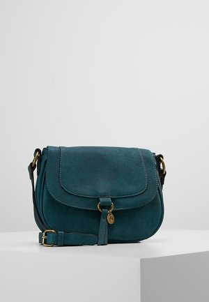 Kožená tyrkysová crossbody taška s klopou, nastavitelným popruhem a zlatým přezkovým a přívěskovým detailem na bílém pozadí.