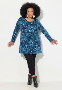 Tunika a maniche lunghe con un motivo astratto blu e nero, abbinata a leggings neri e stivali alla caviglia. Il materiale sembra morbido e con una vestibilità comoda.