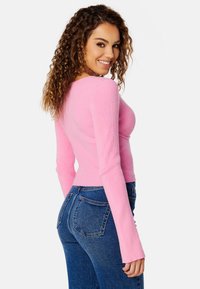 Top a manica lunga aderente a coste di colore rosa brillante, abbinato a jeans in denim blu a vita alta con tasche posteriori e taglio classico.