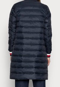 Granatowa puchowa kurtka z poziomymi przeszyciami, o długości do kolan, z kontrastowymi ściągaczami w paski w kolorach czerwonym, białym i niebieskim. Gładka tekstura.