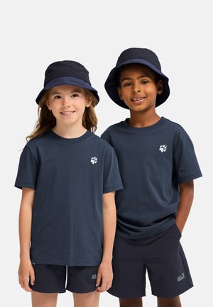 Two smiling children wearing navy bucket hats, matching navy t-shirts with a paw logo, and navy shorts standing against a plain background.