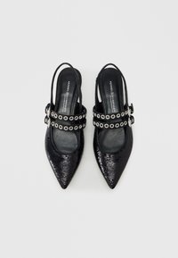 Ζευγάρι μαύρα γοβάκια με μυτερή μύτη και λουράκια slingback, διακοσμημένα με παγιέτες και διπλά πόρπες με ασημένιους κρίκους, τοποθετημένα πάνω σε λευκό φόντο.