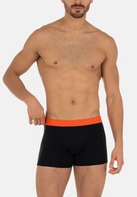Svarta boxershorts med midjeband i orange elastik, med en åtsittande design och mjukt tyg, visade av en manlig modell.