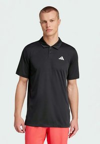 Melnas polo krekls, kas izgatavots no sintētiska materiāla, ar klasisku apkakli, īsām piedurknēm un balto Adidas logo kreisajā krūtīs.