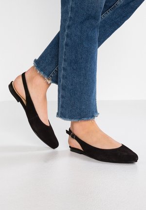 Schwarze Wildleder-Slingback-Ballerinas mit spitzer Spitze, flacher Sohle und schmalem, verstellbarem Knöchelriemen. Getragen mit hellblauen, ausgefransten Jeans.