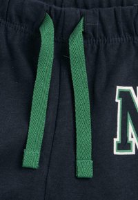 Gros plan sur un tissu bleu marine foncé avec des cordons tressés verts et une lettre partielle "N" blanche et verte imprimée sur le côté droit.