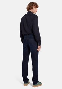 Jeans in denim blu scuro con una vestibilità slim, cuciture dettagliate e due tasche posteriori, abbinati a una camicia nera con bottoni.