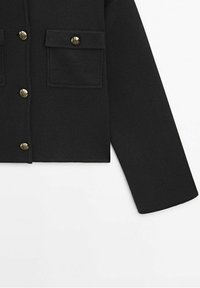 Zwarte gecropte jas van textuurstof, met twee klepzakken en gouden knoppen op een voorflap.