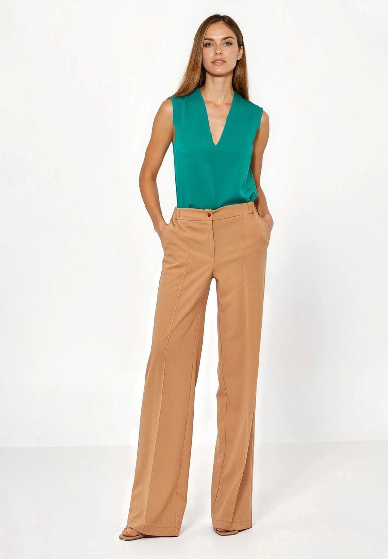 Bluzka bez rękawów w kolorze morskim z dekoltem w serek, zestawiona z wysokim stanem, szerokimi beżowymi spodniami z widocznym czerwonym guzikiem i bocznymi kieszeniami.