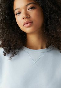 Helles blaues Sweatshirt mit rundem Halsausschnitt und Zierstichen am Kragen, aus einem weichen, strukturierten Stoff gefertigt.
