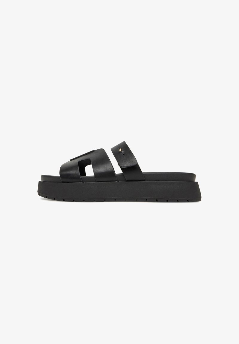 Black leather slide sandal with a thick sole, featuring two wide straps and a cut-out design. Includes a small accent hardware detail.