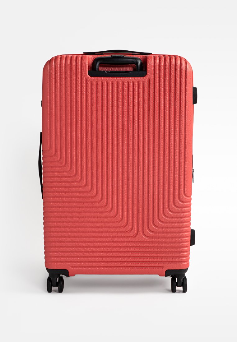 Grande valise rigide rouge avec quatre roues noires et une poignée rétractable noire sur fond blanc.