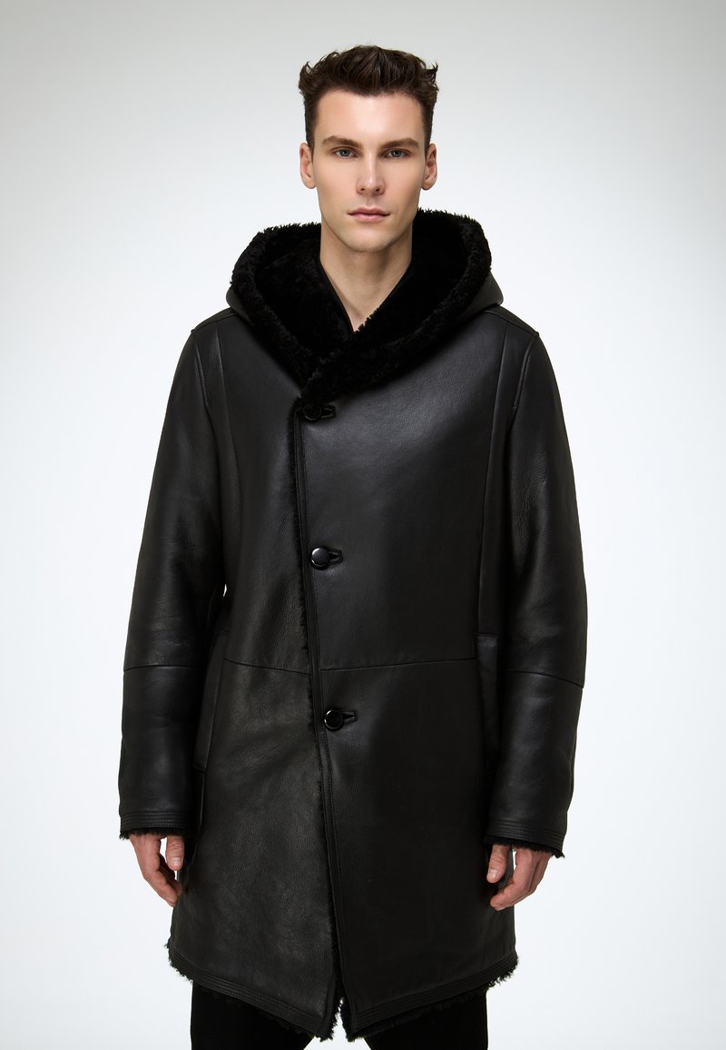 Schwarzer Ledermantel mit großzügiger, flauschiger Kapuze, glatter Textur, Druckknopfverschluss und leicht geschwungenem Saum mit rohen Kanten.