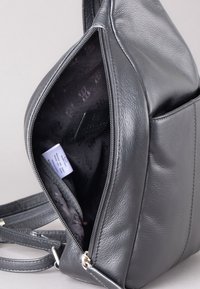 Gray leather bag featuring an exterior zipper, a smooth texture, and a contrasting black patterned interior lining. Adjustable strap visible.