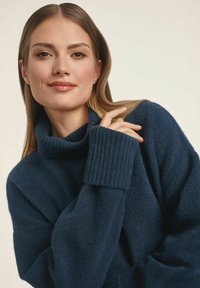 Ciemnoniebieski golf z miękkim, teksturowanym splotem. Posiada prążkowane wykończenia przy mankietach i kołnierzu, co nadaje mu przytulny wygląd.