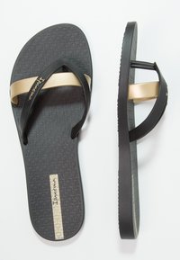 Des tongs noires avec un semelle texturée, dotées d'une bride métallique dorée et d'un logo sur le côté extérieur. Design léger et flexible.