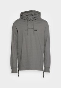 Chemise à manches longues avec capuche en gris discret. Fabriquée en tissu doux, elle est dotée d'un cordon de serrage et comporte un texte imprimé sur la poitrine.