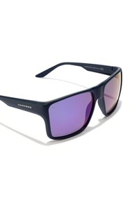 Occhiali da sole blu navy con finitura opaca, forma angolare e lenti color porpora. Presentano il logo 'HAWKERS' sulla regione delle aste. Aste laterali texture.
