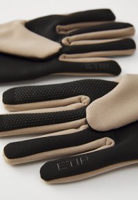 Svarte og beige hansker med teksturert grep på fingertuppene, lettvektig stoff, og det preget merkenavnet "ETIP" på håndleddsområdet.