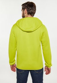 Felpa verde con cappuccio, caratterizzata da una texture liscia e maniche lunghe. Indossata sopra jeans scuri, progettata per un abbigliamento casual.