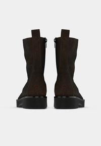 Bottines en daim marron avec une finition texturée, dotées d'une fermeture éclair sur le côté et d'une semelle en caoutchouc noire robuste.