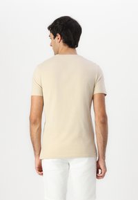 Beige tričko s krátkým rukávem vyrobené z měkké tkaniny, s kulatým výstřihem a slim fit střihem, zobrazené zezadu.